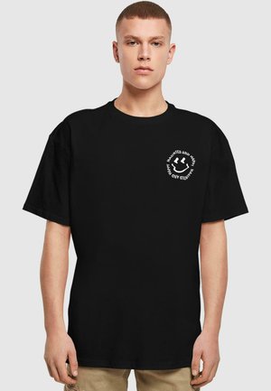 Sort bomulds T-shirt med korte ærmer, rund udskæring og et cirkulært hvidt grafisk tekst på venstre front, der står "Haunted and Happy."