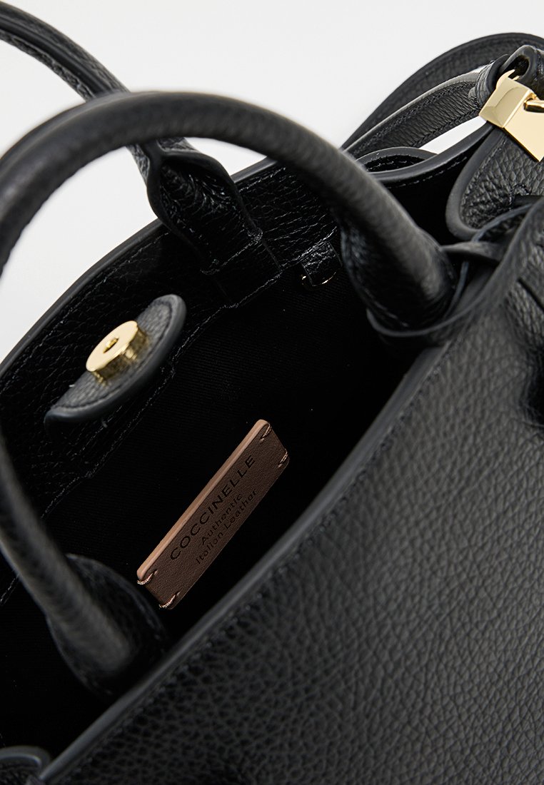 Borsa a mano in pelle nera con texture granitata, accessori in oro e manici corti. L'interno presenta un'etichetta metallica "Coccinelle" su un rivestimento scuro.