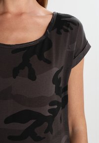 Černé tričko s maskovacím vzorem, s kulatým výstřihem, krátkými ohrnutými rukávy a měkkým bavlněným materiálem. Má volný střih.