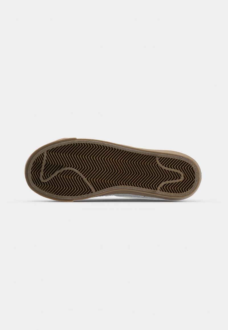 Semelle de chaussure avec un motif en chevrons, base en caoutchouc brun et bord supérieur en textile gris clair. Profil plat sans détails supplémentaires visibles.