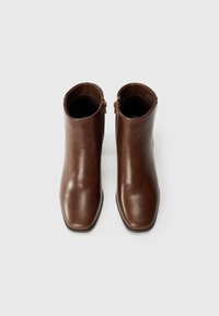 Brown leather ankle boots with a sleek design, square toe, and side zippers. Smooth texture and minimalistic style, suitable for various outfits.