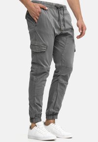 Gray cargo pants with elastic cuffs, front pockets, and side cargo pockets. Made from lightweight fabric with a relaxed fit, paired with white sneakers.