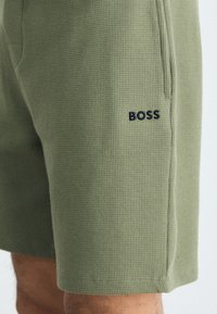 Zelené šortky vyrobené z textúrovaného materiálu, s ryhovaným dizajnom, bočnými vreckami a čiernym logom "BOSS" na ľavom stehne.