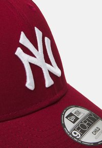 Gorra de béisbol roja con visera curvada, que presenta un logo NY bordado en blanco en la parte frontal. Incluye una pegatina redonda de New Era.