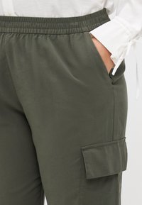 Ελαιοπράσινα cargo παντελόνια με ελαστική μέση, πλαϊνή τσέπη και τσέπη με καπάκι στο μηρό. Λείο, ελαφρύ ύφασμα.