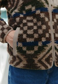 Brown and beige patterned fleece jacket with blue and green accents; features a soft texture, contrasting beige trim, and side pockets.