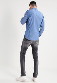 Lichtblauw denim shirt met een ronde onderkant, gecombineerd met donkergrijze jeans, gedragen met witte sneakers. Het shirt heeft een standaard kraag en knoopsluiting.