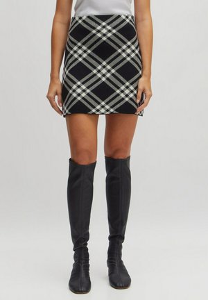 Jupe mini en tricot avec un motif à carreaux noir et blanc, dotée d'une coupe près du corps. Associée à de longues bottes en cuir noires pour créer un contraste.