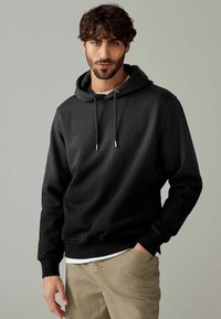Black hoodie with a drawstring, made of soft cotton blend fabric. Features ribbed cuffs and hem, worn over a white shirt, with a relaxed fit.