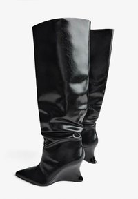 Čierne vysoké kožené čižmy s lesklým povrchom, so špicatou špičkou a klinovým podpätkom. Majú nastrihovanie pozdĺž holennej časti.