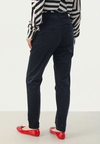 Navy corduroy pants with a tapered fit, featuring back pockets. Paired with red ballet flats, viewed from the back.