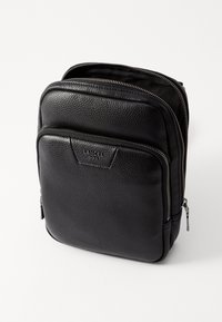 Sac à dos en cuir noir avec une finition texturée, deux compartiments zippés et un logo de marque discret à l'avant.