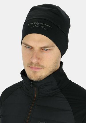 Black beanie with "SWEDEMOUNT" logo and mountain design on the front, made of a smooth, stretchy fabric, fitted to the head.