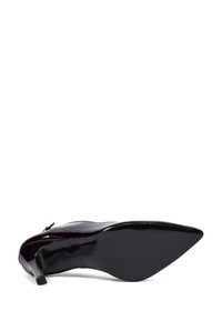 Zapato de tacón alto de charol negro con punta afilada, tacón delgado y un sutil detalle de cremallera en el lateral. Textura suave y brillante.