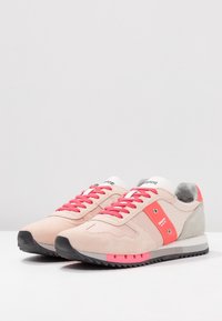 Zapatillas deportivas de color rosa claro con detalles en coral, material de ante y malla, etiqueta blanca, suela gruesa negra y detalle texturizado en el talón gris.