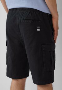 Schwarze Cargo-Shorts mit elastischem Bund, Seitentaschen und einer Gesäßtasche mit Etikett. Der Stoff hat eine dezente, strukturierte Oberfläche.