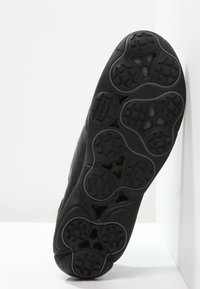 Tenis negri cu o talpă din cauciuc texturat, având un model de profil. Materialul superior neted se întinde în jurul unei secțiuni modelate a călcâiului.