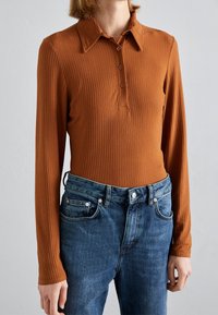 Long-sleeve ribbed top in burnt orange with a collar and three buttons, paired with mid-rise dark blue denim jeans featuring front pockets.