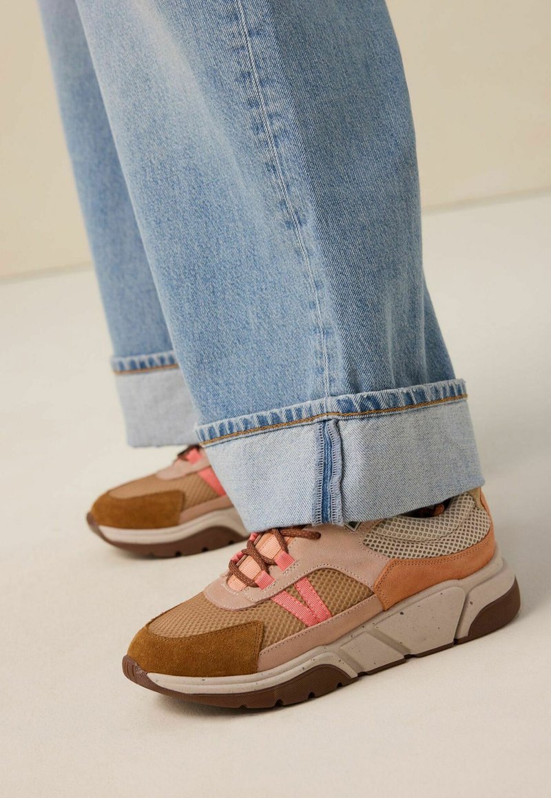 Baskets marron et roses avec un tissu en mesh, des accents en daim et une semelle texturée, associées à un jean léger en denim bleu clair retroussé.