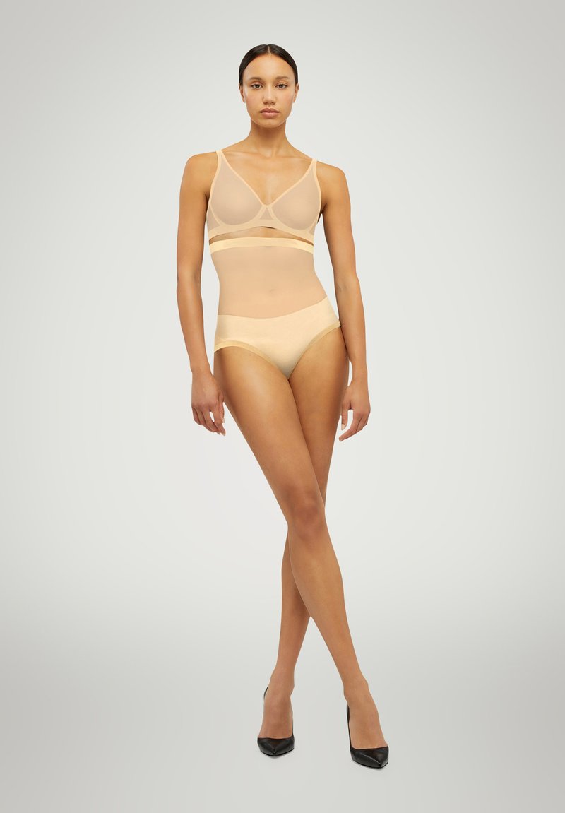 Nude mesh underkläder set bestående av en bralette med dekorativa remmar och matchande högmidjade trosor. Slät textur och minimalistisk design.