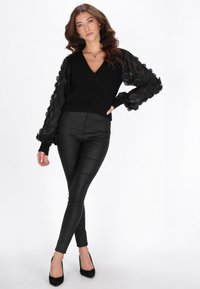 Maglione nero con maniche a palloncino trasparenti e testurizzate, abbinato a pantaloni aderenti neri in ecopelle e tacchi neri. Tessuto liscio, design con scollo a V.