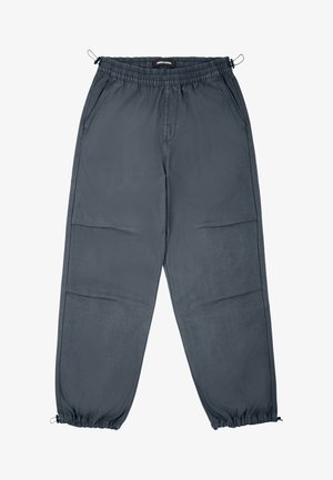 Pelēki džogeri ar elastīgu jostu, sānu kabatām un elastīgiem manšetes galiem, ar gludu tekstūru un taisnu piegriezumu.