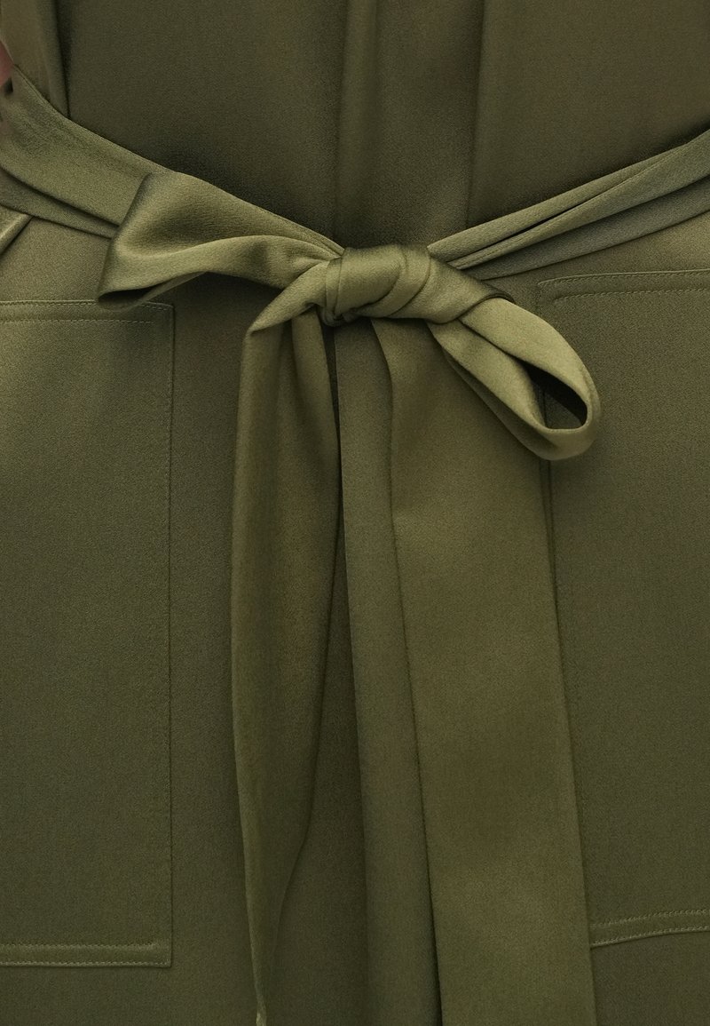 Olive green garment with a smooth texture, featuring a tied belt at the waist and two patch pockets on the front.
