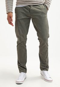 Zielone lekkie chinosy o prostym kroju, z przednimi kieszeniami, w połączeniu z białymi trampkami. Gładka tekstura materiału.