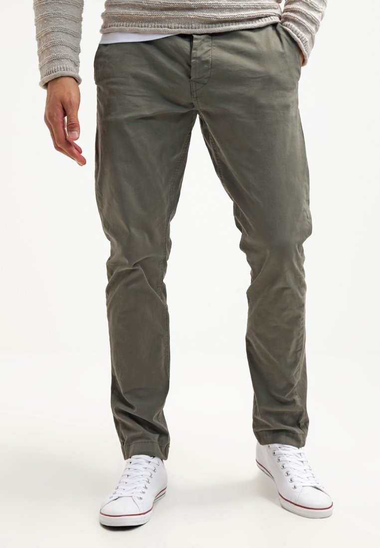 Zielone lekkie chinosy o prostym kroju, z przednimi kieszeniami, w połączeniu z białymi trampkami. Gładka tekstura materiału.