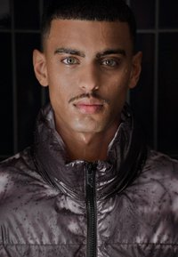 Vodootporna, tamnosiva jakna s kapuljačom i prednjim patentnim zatvaračem. Ima kišne kapi na površini, pokazujući glatku teksturu.