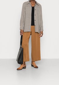 Gekruiste blouse met lange mouwen, zwarte v-hals top, beige wijde broek, bruine enkellaarsjes en een zwarte tote bag. Eenvoudige, gelaagde outfit.