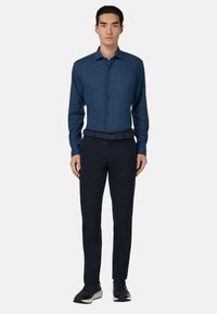 Granatowa koszula z długim rękawem, z kołnierzykiem zapinanym na guziki oraz fakturowanym materiałem. Połączona z ciemnymi spodniami i granatowym paskiem o fakturze.
