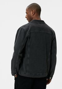 Zwarte denim jacket met een klassieke kraag, lange mouwen en knoopmanchetten. De stof heeft een gladde textuur met subtiele vervagingseffecten.