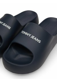 Chanclas de goma azul marino con los dedos al aire y una suela elevada, que presentan "TOMMY JEANS" impreso en blanco en la correa.