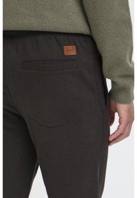 Zwarte joggingbroeken met een gladde textuur, voorzien van een achterzak en een leren label met de tekst "BLEND." Gecombineerd met een groene trui.