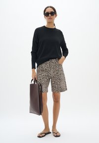 Pull noir, short beige à imprimé léopard, lunettes de soleil opaques, sac fourre-tout marron et tongs noires. Design simple avec des motifs contrastés.