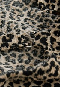 Tkanina s leopard uzorkom s bež pozadinom i crnim mrljama. Uključuje nabranu teksturu i metalne detalje u obliku prstenova.