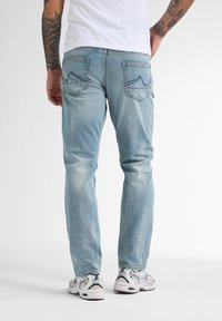 Jeans azzurri chiari in denim, con una linea dritta, dettagli sbiaditi e due tasche posteriori con accenti cuciti. Indossati con scarpe da ginnastica bianche.