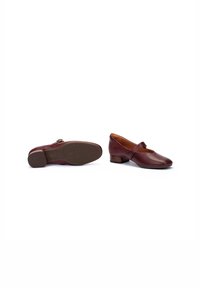 Zapatos de cuero burdeos con puntera redonda y detalle de correa, que cuentan con un tacón bajo y suela de goma texturizada. Acabado plano y suave.