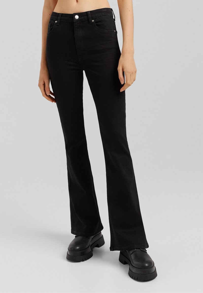 Mustat leveälahkeiset farkut, jotka on valmistettu denimistä, sisältävät puolivälin vyötärön, viisi taskua, hopeiset yksityiskohdat ja pienehkön joustavuuden mukavuutta varten.