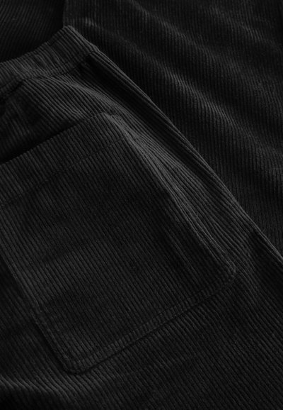 Gros plan sur un tissu en velours côtelé noir montrant une poche rectangulaire avec des côtes verticales visibles et des bords cousus.
