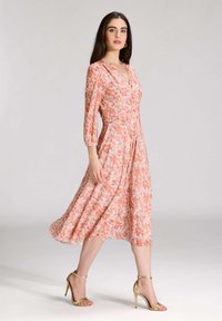 Kukallinen midi-mekko V-pääntiellä ja kolmannen osan hihoilla, vaaleanpunaisen ja oranssin sävyissä, jossa on vartalonmyötäinen yläosa ja valuvampi helma.
