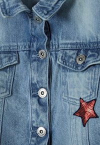 Džínová bunda v světle modré barvě, s stříbrnými patentkami a dvěma předními kapsami. Výrazná nášivka hvězdy z červených flitrů na pravé straně.