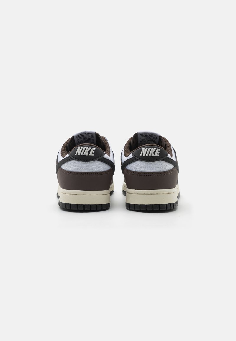 Des baskets Nike avec une base en cuir marron, des accents en maille blanche et des semelles en caoutchouc noir. La vue arrière met en avant le logo et les détails de couture.
