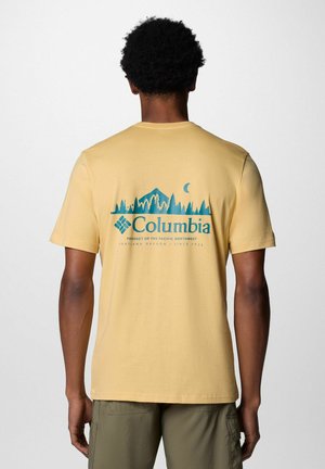 T-shirt in cotone giallo chiaro con una grafica blu di montagne e alberi sul retro, con il testo e il logo "Columbia" vicino al colletto.