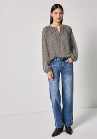 Lettet, langærmet bluse i et sort og beige dyreprint, parret med afslappede blå jeans og sorte ankelstøvler.
