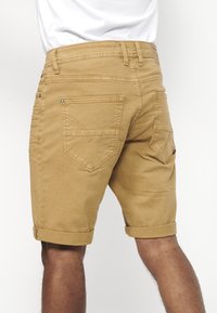 Shorts kaki avec ourlets retroussés, fabriqués en coton texturé. Comprend des poches arrière et des accessoires en métal. Design simple sans motifs visibles.