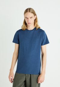 Granatowa koszulka z krótkim rękawem z miękkiej bawełny, z okrągłym dekoltem i prostym krojem, w połączeniu z oliwkowymi spodniami.