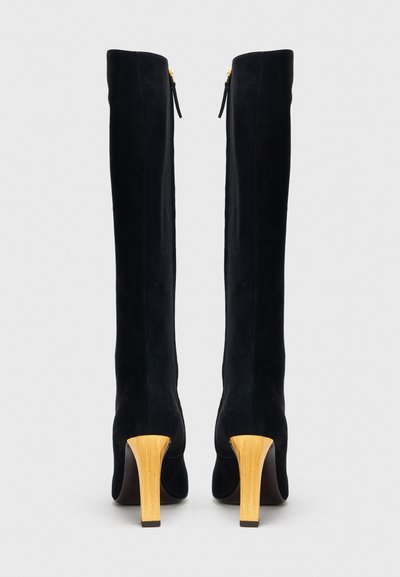 Térdig érő fekete színű szarvasbőr csizma sima textúrával és aranyszínű cipzárakkal, jellegzetes fa blokk sarokkal.