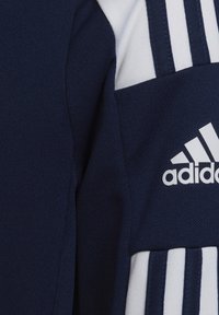 Giacca sportiva blu navy con accentuazioni bianche, realizzata in tessuto testurizzato, con tre strisce bianche sulla spalla e logo Adidas.